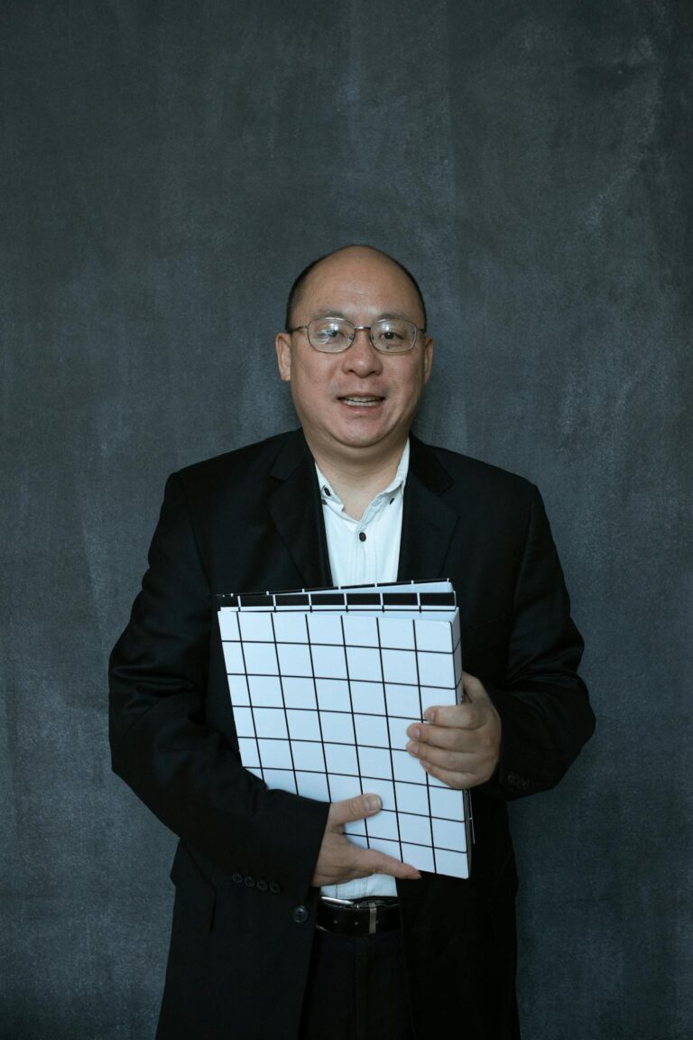 Confident man in a suit holding a document folder against a dark backdrop.